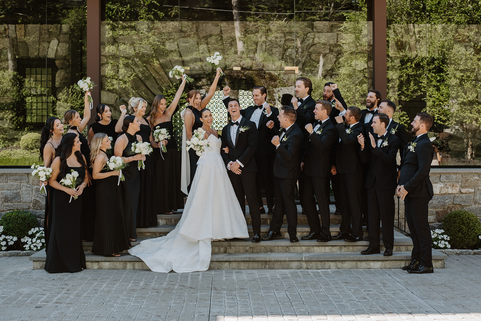 Wedding party in black attire cheering and celebrating on steps outside Le Chateau.